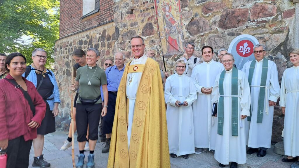 Arkkipiispa yhdessä messun toimittajien kanssa liturgisessa vaatetuksessa Turun tuomiokirkon portailla. Kuvassa myös pyhiinvaeltajia.