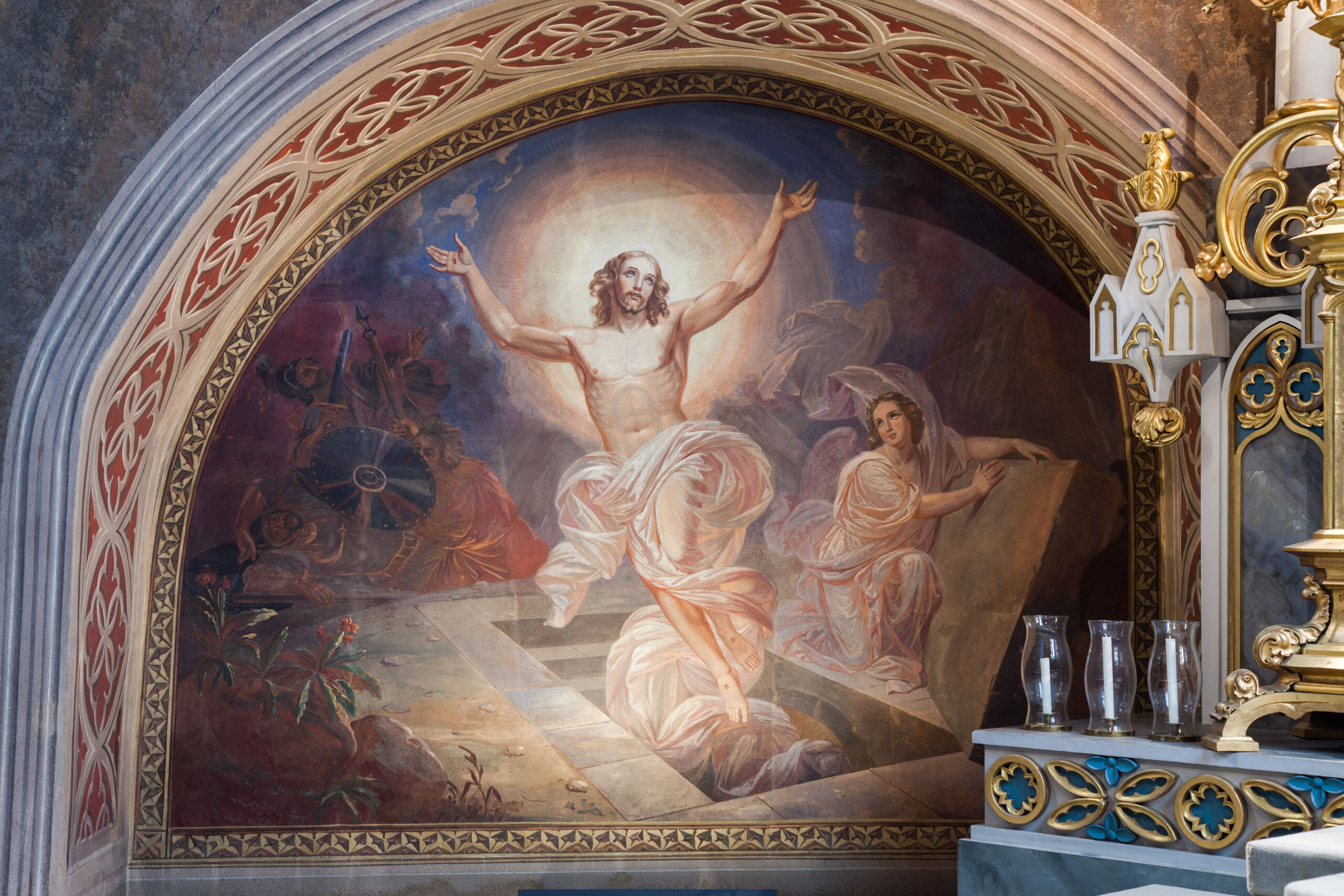 Jesus stiger upp ur graven, vita svepningar täcker hans underkropp, överkroppen och bakom huvudet finns en ljus gloria. Bredvid lutar en ängel sig mot gravstenen som tagits bort från graven och tittar på den uppståndne Jesus.